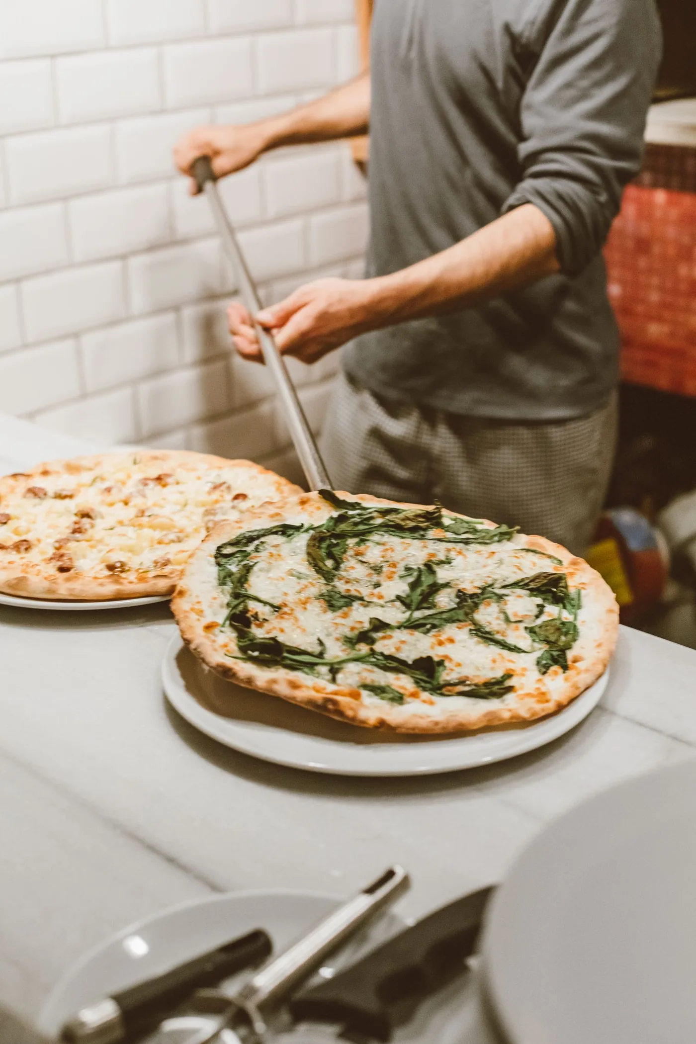 Pizzaiolo sliding a pizza into the wood-fired oven at Forno YYC